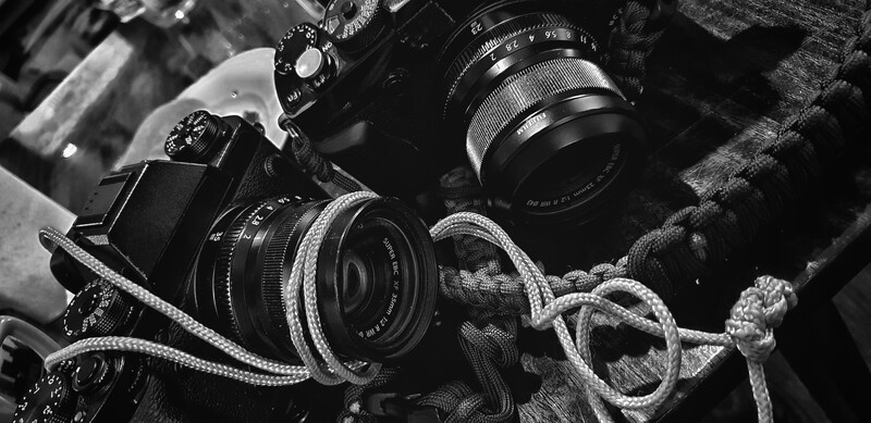 Vintage camera equipment and lenses arranged on textured fabric in black and white.