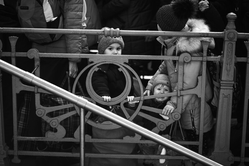 Black and white photograph of two young children peering through a ship's wheel while standing at a railing.
