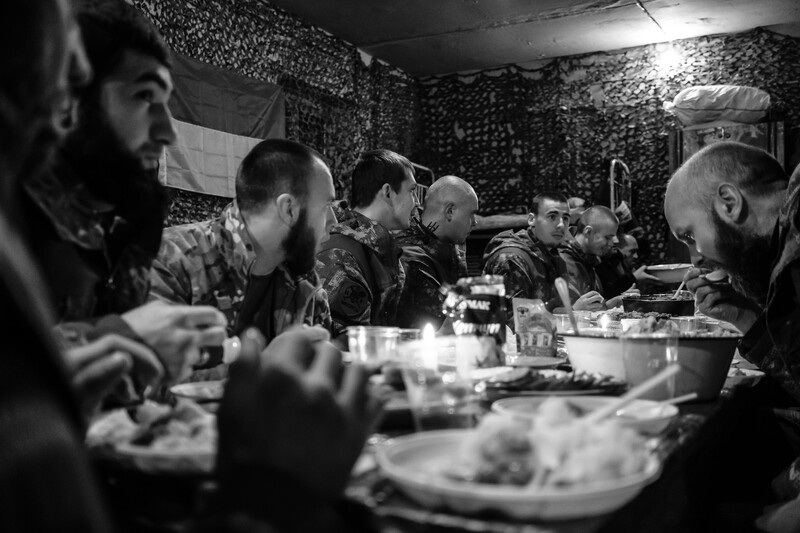 Soldiers sharing a meal together in a tent with camouflage netting overhead.