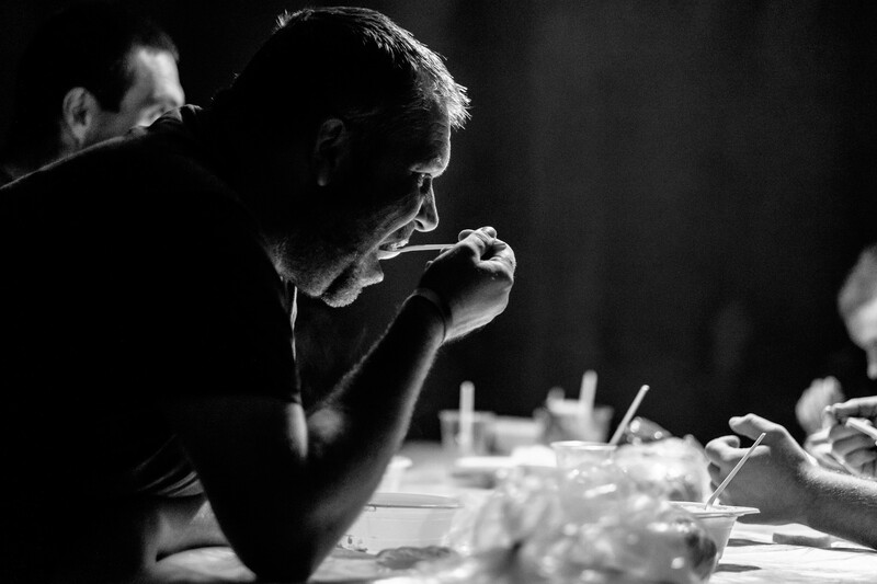 Man eating at a table during what appears to be a social gathering, shot in high-contrast black and white.