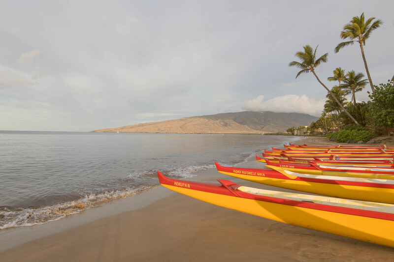 Red and yellow kayaks lined up on a sandy beach with calm water and a distant volcanic island.