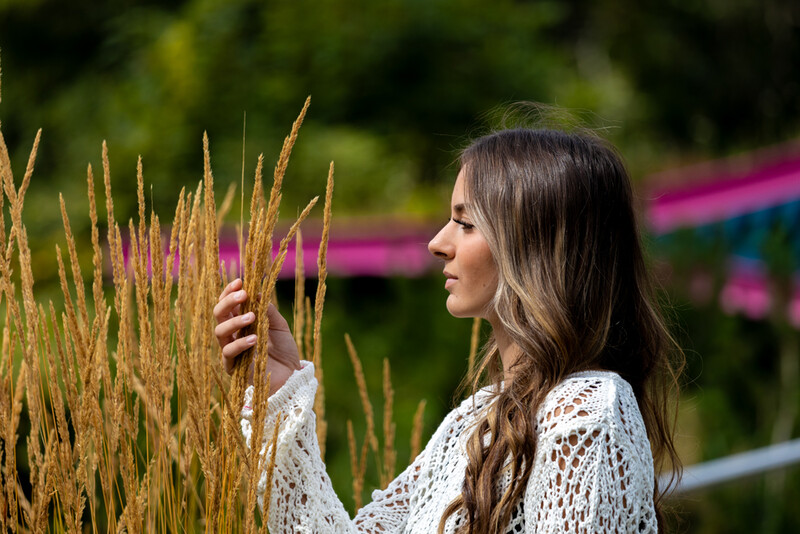 Woman in white lace cardigan touching golden grain stalks in a garden setting.