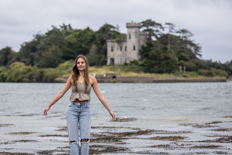 Woman standing in shallow water with a castle visible across the bay behind her.