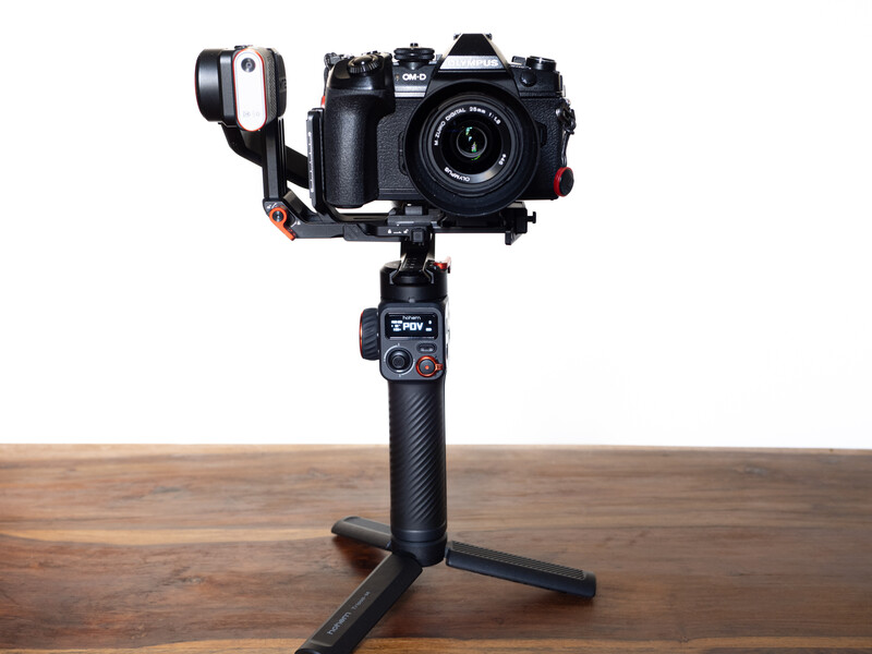 Professional camera gimbal with mounted mirrorless camera and wireless microphone on wooden surface.