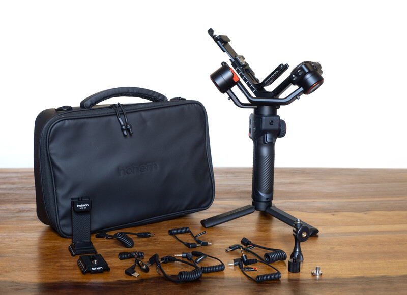Three-axis gimbal stabilizer with carrying case and accessories on wooden surface.