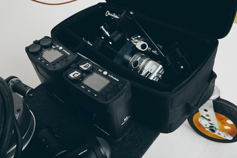 Open camera bag displaying professional video equipment including cinema camera, lenses, and wireless microphone transmitters on white background.