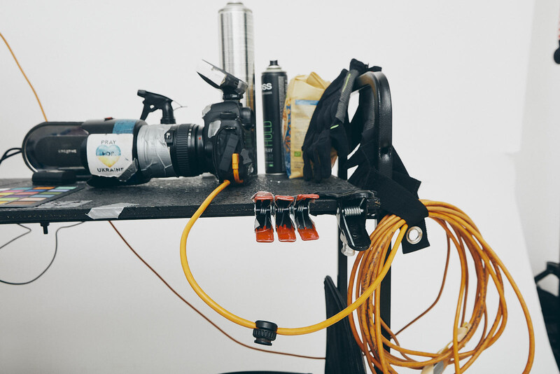 Camera equipment and cables organized on a wall-mounted shelf with yellow extension cord coiled below.