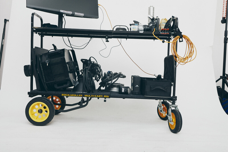 Custom production cart with yellow and black wheels, mounted monitor, lighting equipment, and cable management on white background.