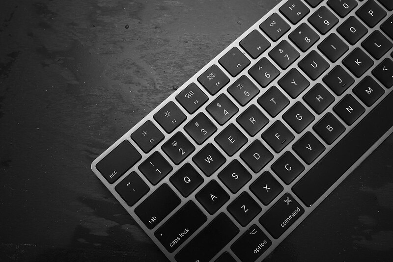 Angled overhead view of a silver wireless keyboard on a dark textured surface.