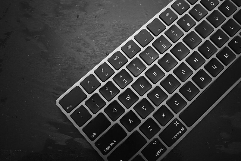 Angled view of a silver and black wireless keyboard on a dark textured surface.