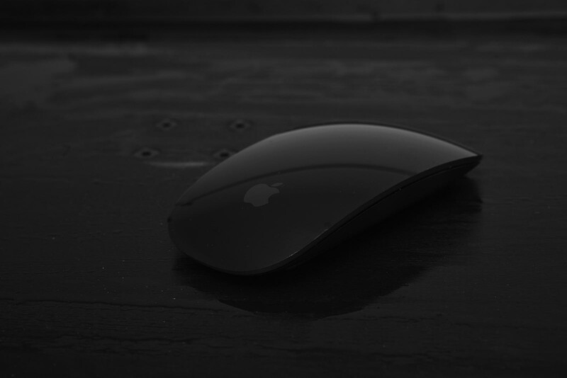 Wireless computer mouse with curved ergonomic design on dark wooden surface.