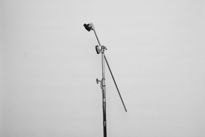Studio light stand with mounted reflector and boom arm against neutral background.
