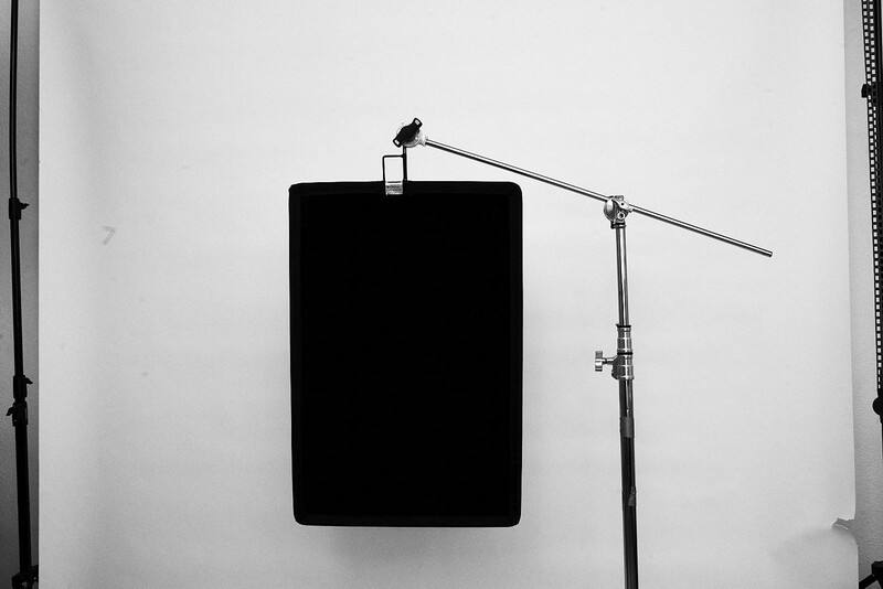 Studio lighting setup with a boom arm extending from a black rectangular reflector or diffusion panel against a white backdrop.