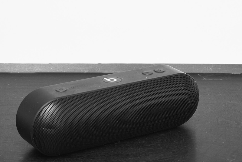 Black wireless speaker positioned on a dark surface against a light background.