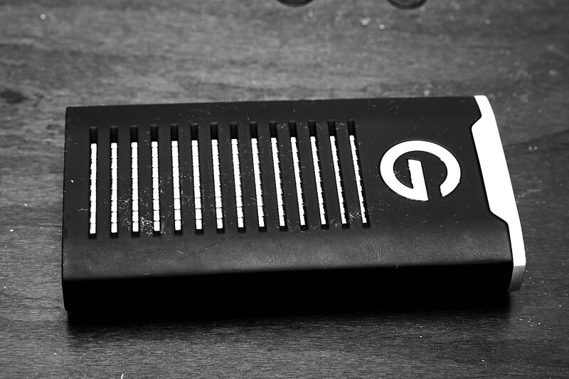 Black rectangular device with white vertical lines and a circular logo on dark textured surface.