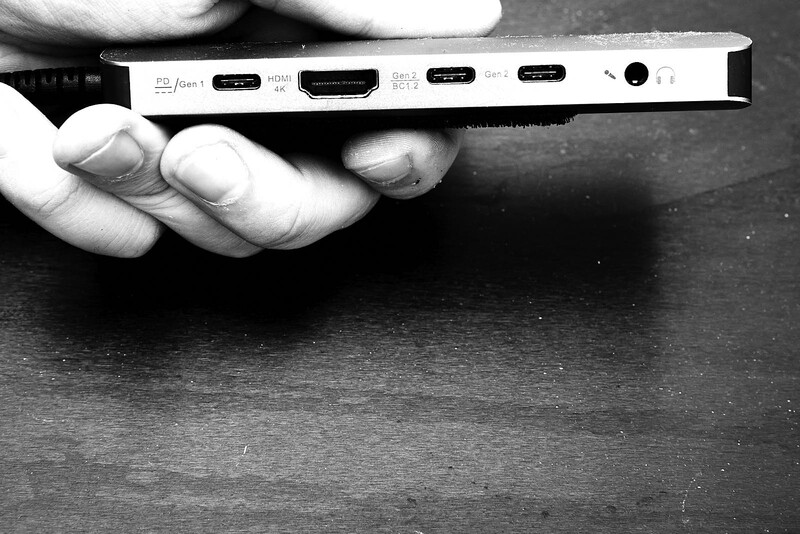 Hand holding a white device showing multiple ports including HDMI, USB-C, and audio jack.