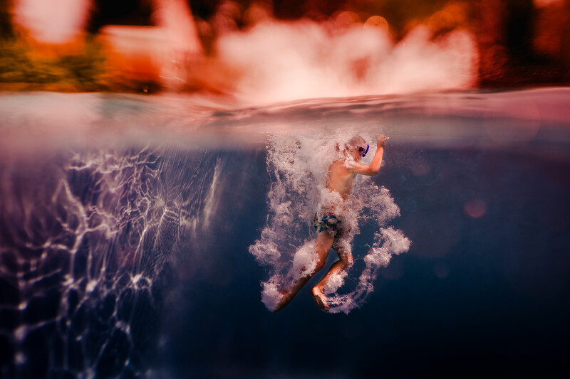 Underwater split-view of a figure suspended in water with bubbles rising, surrounded by an intricate web-like structure.