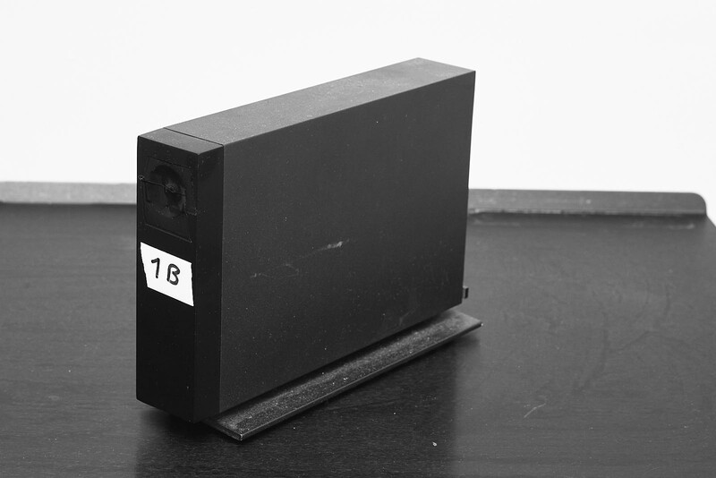 External hard drive with 1TB label standing upright on dark surface with stand.