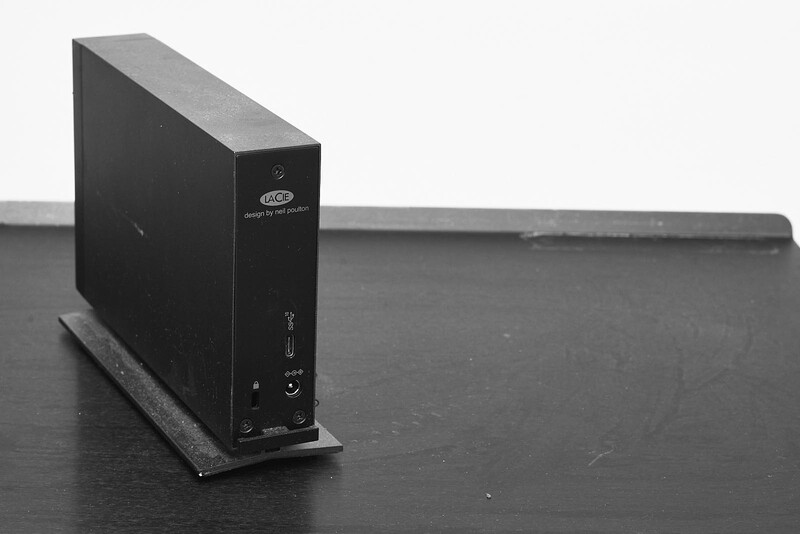 Black external hard drive or storage device on a dark wooden surface with cable connections visible.