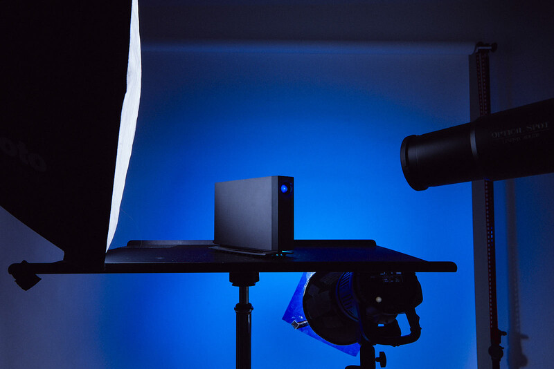 Studio setup with laptop on desk, professional lighting equipment, and blue backdrop illumination.