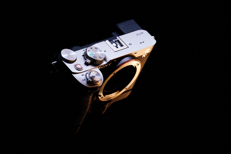 Vintage rangefinder camera with champagne-gold body and white top plate, shot against black background.