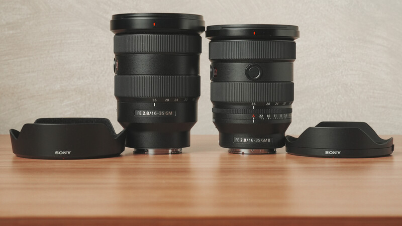 Two Sony mirrorless camera lenses with attached lens hoods displayed on wooden surface.