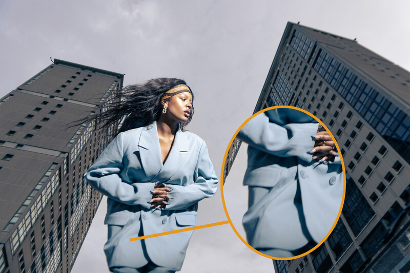 Woman in light blue blazer jogging between tall buildings with circled detail of fabric texture.