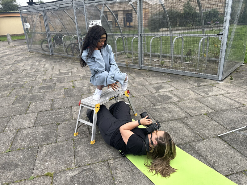 Fitness instructor demonstrating an abdominal exercise on a client using a yellow and white step platform outdoors.