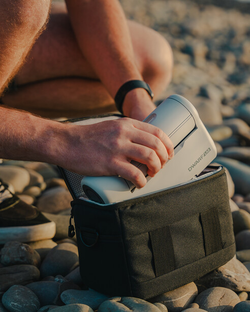 Hands holding an open notebook while sitting on sandy ground outdoors.