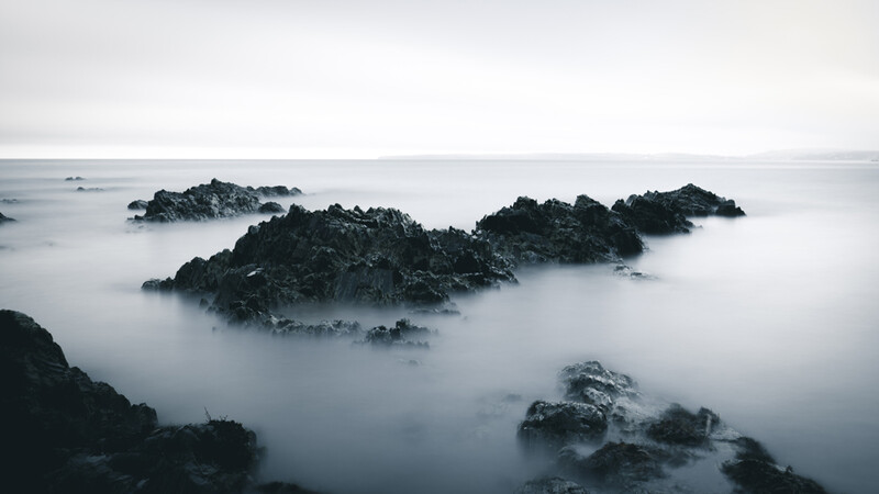 Rocky islands shrouded in mist rising from calm, gray ocean water.