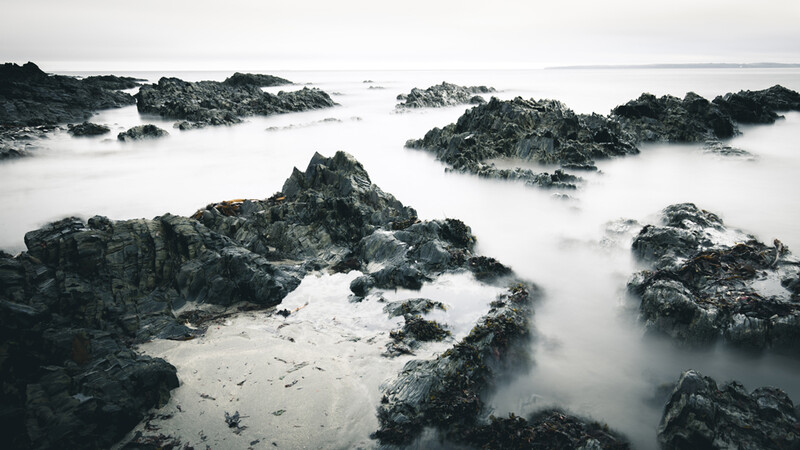 Rocky coastal formations partially submerged in heavy sea mist during high tide.