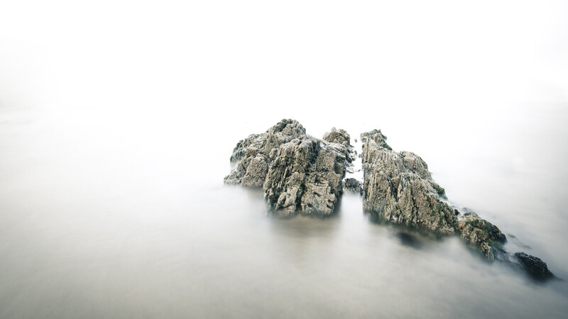 Rocky mountain peaks emerging from dense fog and mist against an overcast sky.