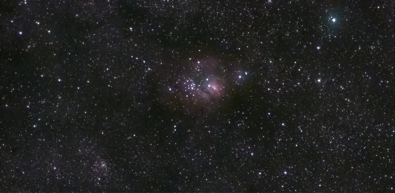 Deep sky photograph showing a nebula cluster with bright stars and colorful gas emissions against a dark starfield.