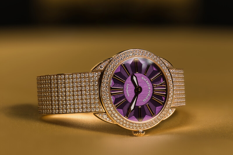 Luxury watch with purple dial, diamond-set bezel, and mesh band against warm gold background.