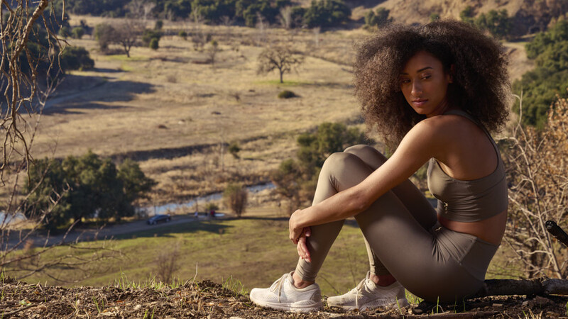 Woman with curly hair sitting on hillside overlooking pastoral valley landscape.