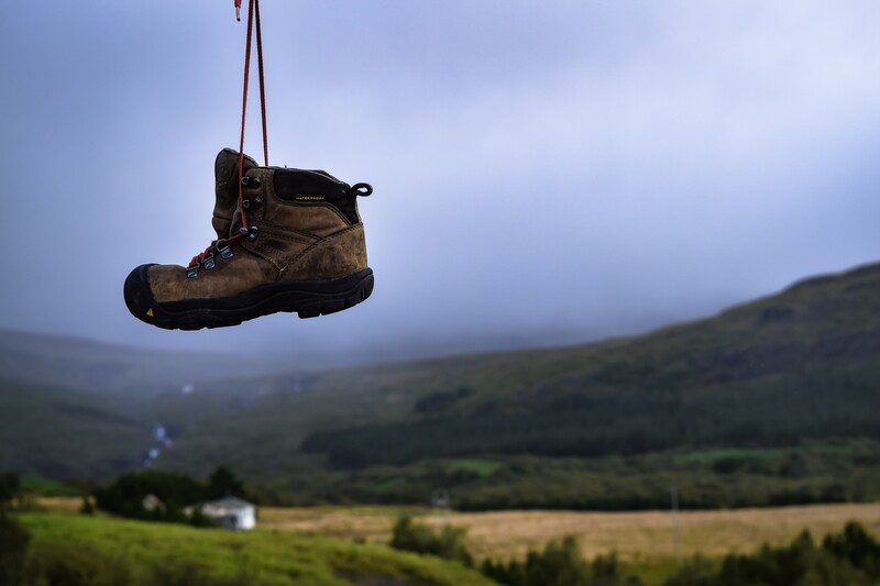 Worn hiking boot suspended by a lace above a misty valley landscape.
