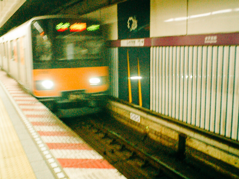 A subway train with illuminated headlights arriving at a station platform with safety barriers.