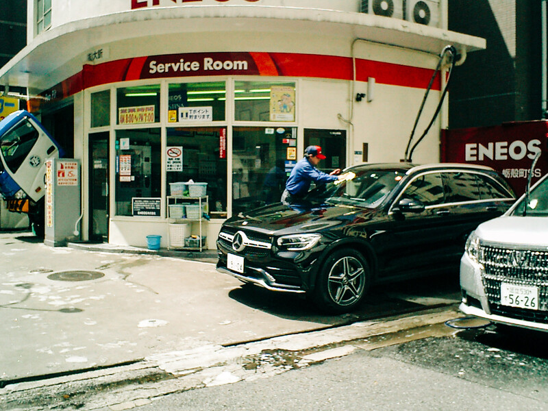Black sedan parked at an ENEOS service station with attendant visible near the storefront.