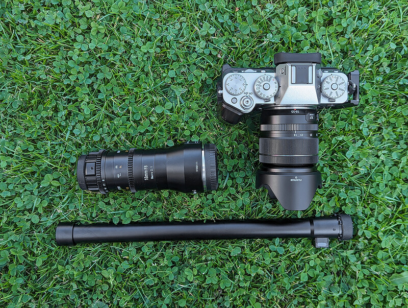 Mirrorless camera body with telephoto lens and lens hood arranged on green grass.