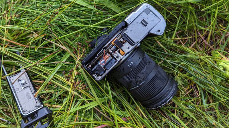 Mirrorless camera with attached telephoto lens lying on grass next to a battery pack.
