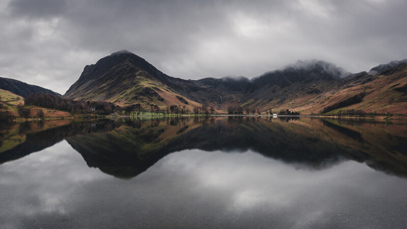 Dramatic mountain landscape reflected perfectly in still lake water under overcast sky.