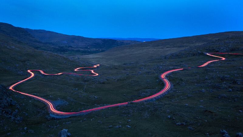 Glowing lava streams flow down dark volcanic slopes under twilight sky.