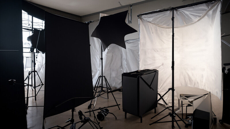 Professional photography studio setup with black flags, softbox reflectors, and lighting stands arranged around a black product box.