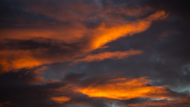 Dramatic sunset sky with golden-orange clouds backlit against dark storm clouds.