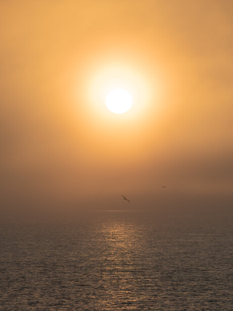 Bright sun burning through hazy atmospheric conditions above a calm ocean horizon.