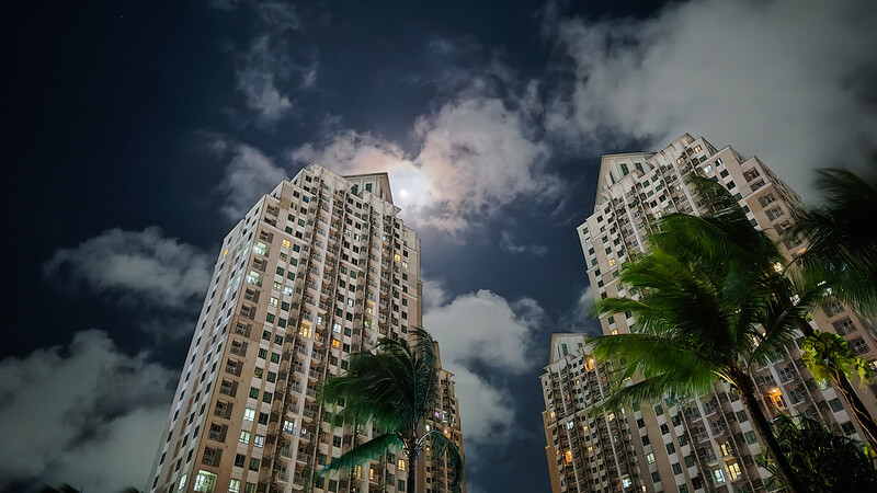 Tall residential apartment buildings shot from below against a dramatic blue sky with white clouds and palm fronds visible.