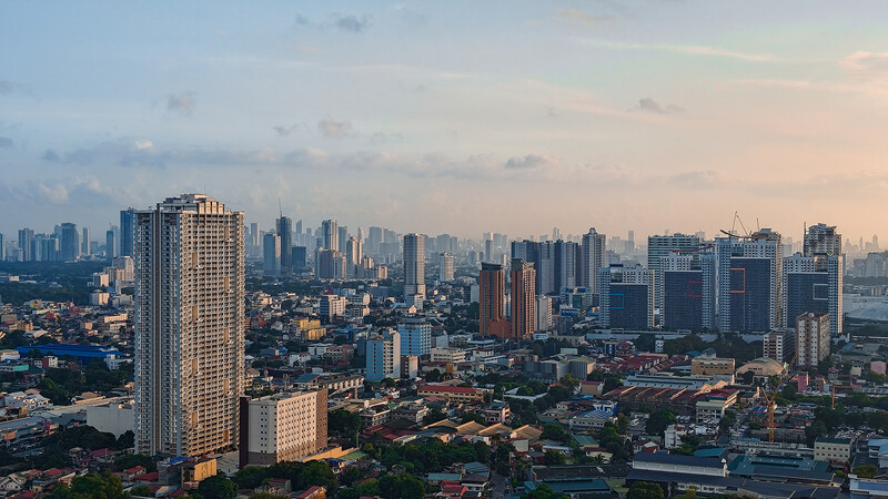 Dense urban skyline at golden hour with a tall residential tower in the foreground casting warm light across the cityscape.