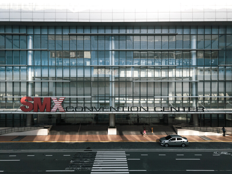 Modern glass-facade building with red signage and a white crosswalk, car waiting at street level.