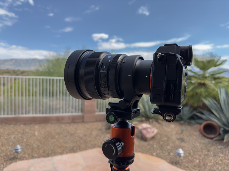 Mirrorless camera with telephoto lens mounted on red ball head tripod outdoors.