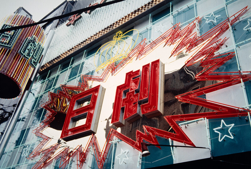 Vintage neon sign with red lettering and lightning bolt design against a modern building facade.